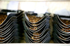 A stack of metal scoops, each containing KENYA NGUNGURU roasted coffee beans.