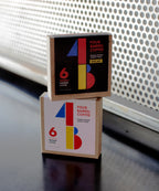 Two square boxes of INSTANT COFFEE with colorful geometric designs stacked on a dark surface.