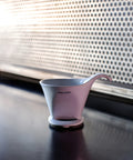Pink coffee dripper on a dark surface with a patterned wall in the background