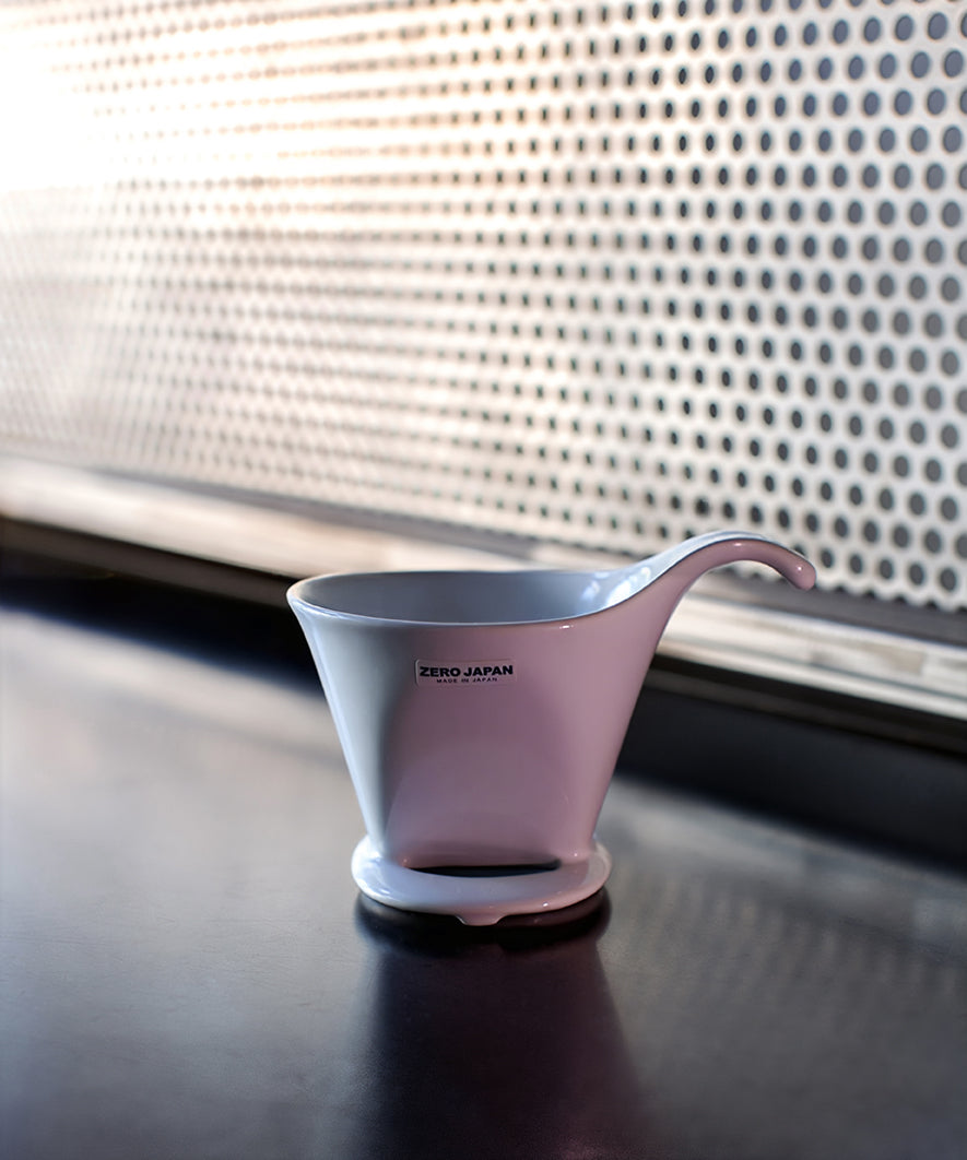 Pink coffee dripper on a dark surface with a patterned wall in the background