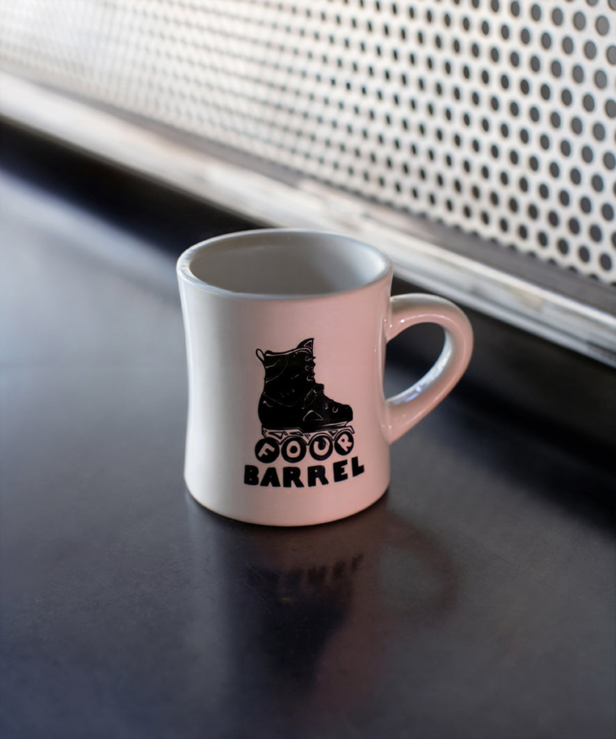 Pink mug with roller skate design and 'Roller Barrel' text on a dark surface.