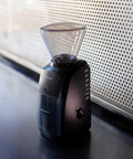 Black coffee grinder with clear top on a dark surface, blurred background