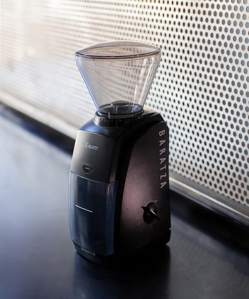 Black coffee grinder with clear top on a dark surface, blurred background