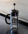 French press coffee maker on a reflective surface with a textured wall in the background