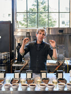 Man standing behind a counter with coffee samples in a coffee shop setting