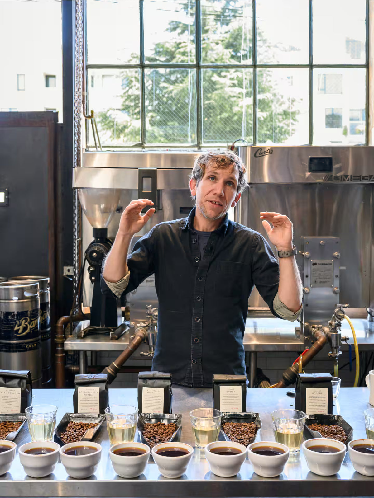 Man standing behind a counter with coffee samples in a coffee shop setting