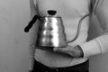 A person holding a Hario Buono Kettle, a stainless steel gooseneck kettle with a ribbed body and black handle.