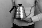 A person holding a Hario Buono Kettle, a stainless steel gooseneck kettle with a ribbed body and black handle.