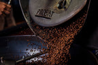 FRIENDO BLENDO ESPRESSO coffee beans pouring from a metal industrial roaster.