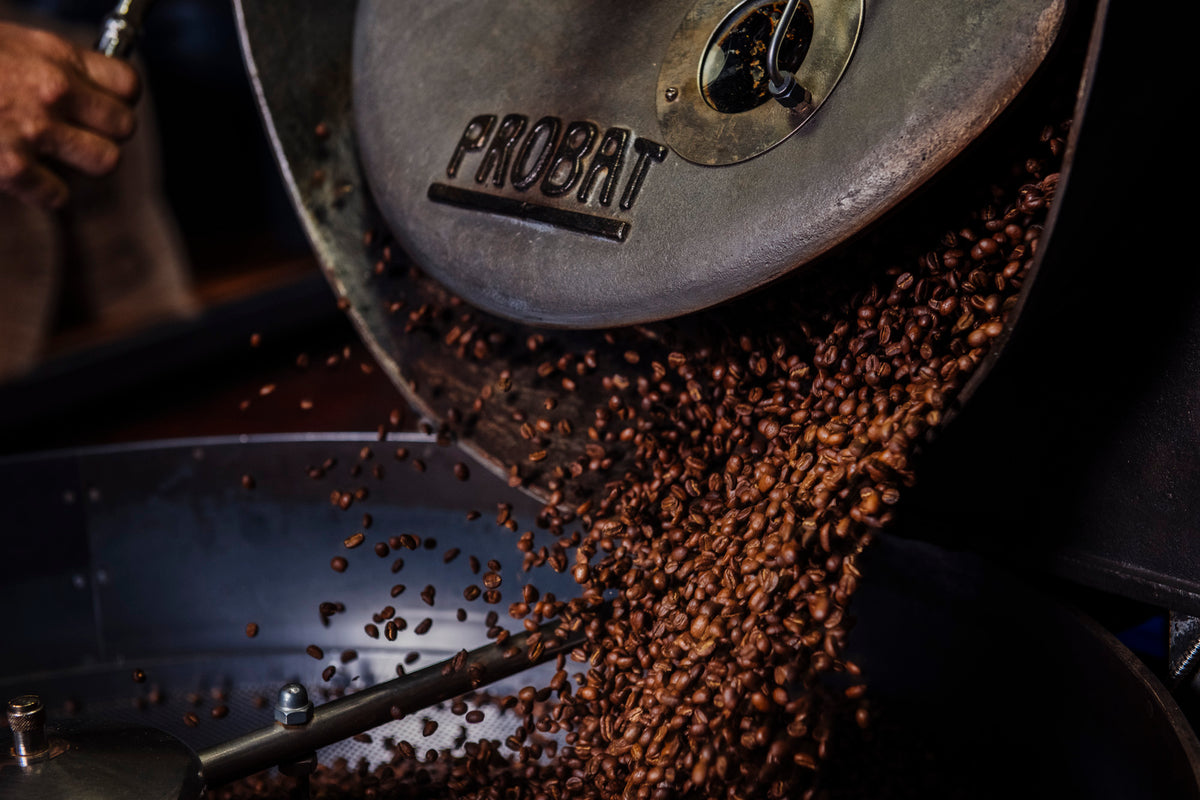 FRIENDO BLENDO ESPRESSO coffee beans pouring from a metal industrial roaster.