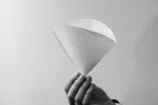 A hand holding a white conical Hario Paper Filters #02.