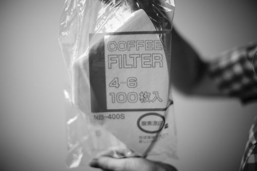 A hand holds a plastic package of 100 white Bonmac #4 White Paper Filters.