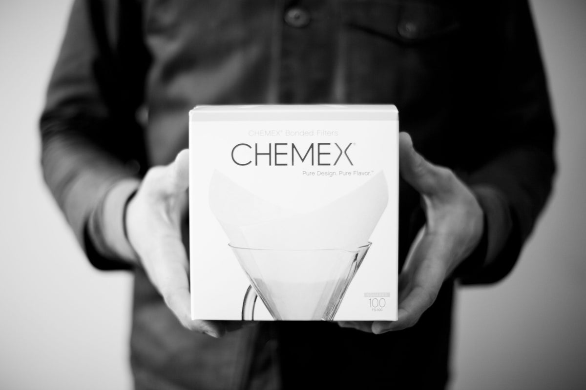A person holds a square box of Chemex 8 Cup Filters featuring an illustration of a pour-over coffee maker.