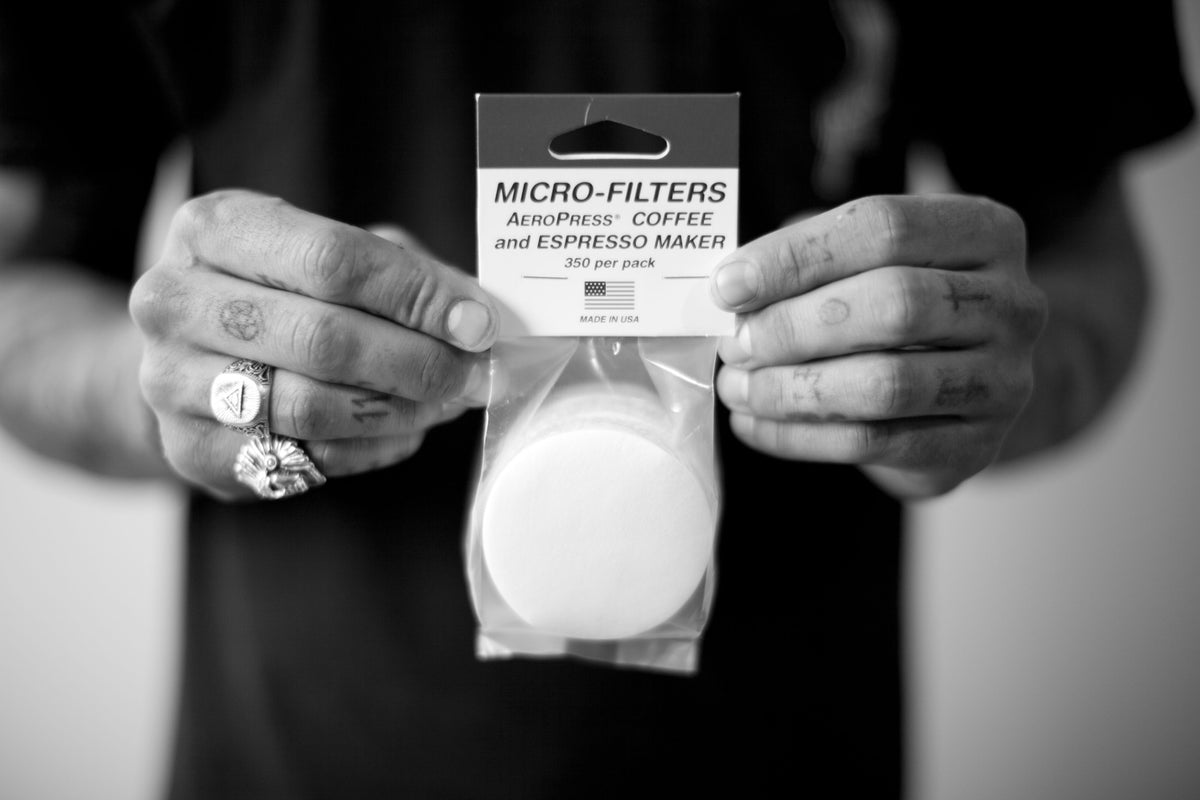 Hands holding a plastic bag containing a stack of circular AEROPRESS FILTERS.