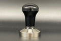 A stainless steel tamper with a black power-coated handle, designed by Reg Barber.