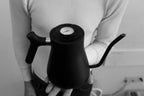 Person holding a black Fellow Stagg Stove Top Pour Over Kettle with a temperature gauge on the lid.