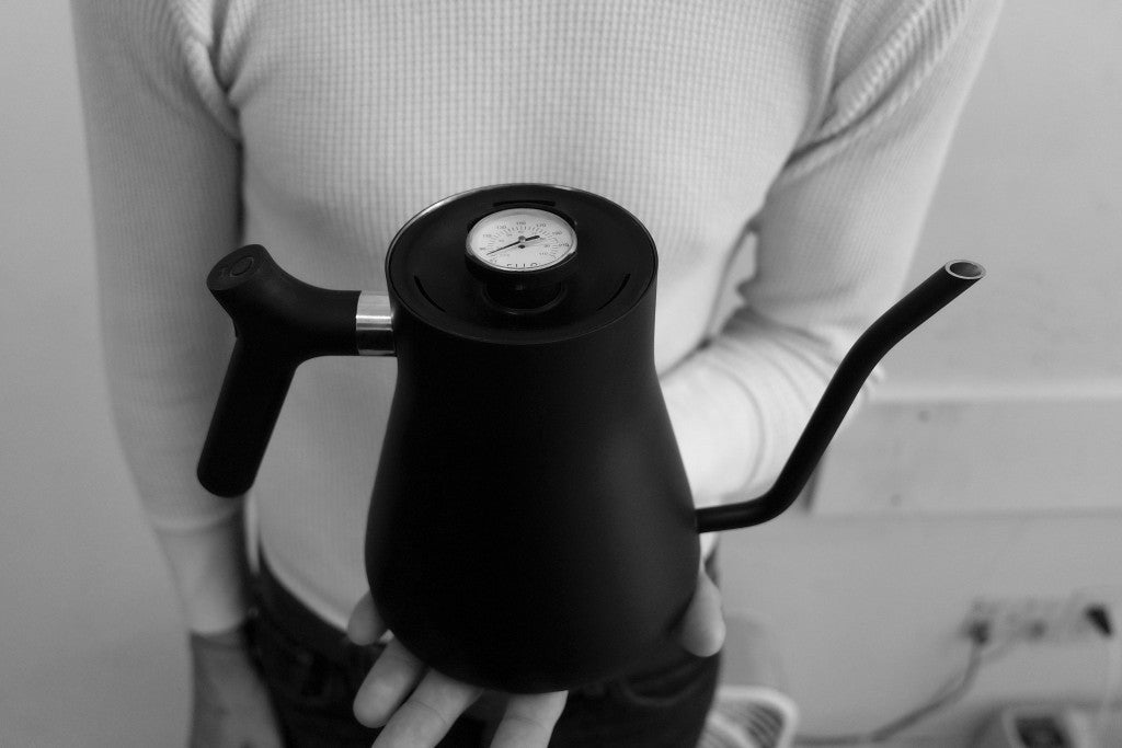 Person holding a black Fellow Stagg Stove Top Pour Over Kettle with a temperature gauge on the lid.