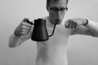 A person in glasses holds a black Fellow Stagg Stove Top Pour Over Kettle to their mouth as if tasting from the spout.