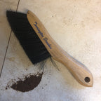 A torrington wood counter brush with black bristles lying on a tiled surface next to a small pile of dark debris.