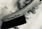 Hand holding a torrington wood counter brush with a wooden handle and black bristles being used to sweep debris.